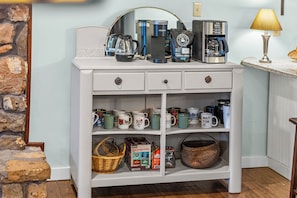 A white wooden cabinet with multiple shelves, containing various coffee makers, mugs, and coffee-related items.