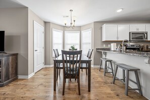 A modern kitchen with white cabinets, a microwave, and a dining area with a wooden table and chairs.