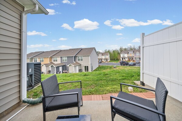 A patio with two chairs and a table, a grassy yard, and a row of townhouses in the background.