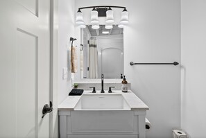 Une salle de bain avec un lavabo blanc, un robinet noir et un miroir surmonté de lampes.