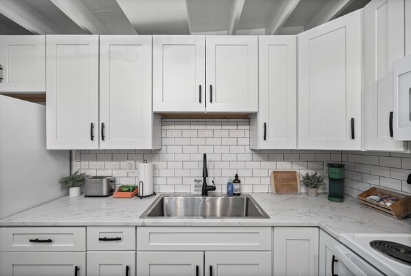 A kitchen with white cabinets, a stainless steel sink, and a marble countertop.