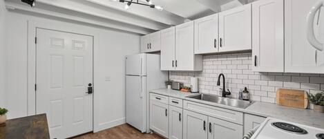 Una cocina moderna con armarios blancos, un lavamanos de acero inoxidable, una estufa y una encimera de madera.
