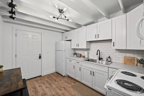 A modern kitchen with white cabinets, a stainless steel sink, a stove, and a wooden countertop.
