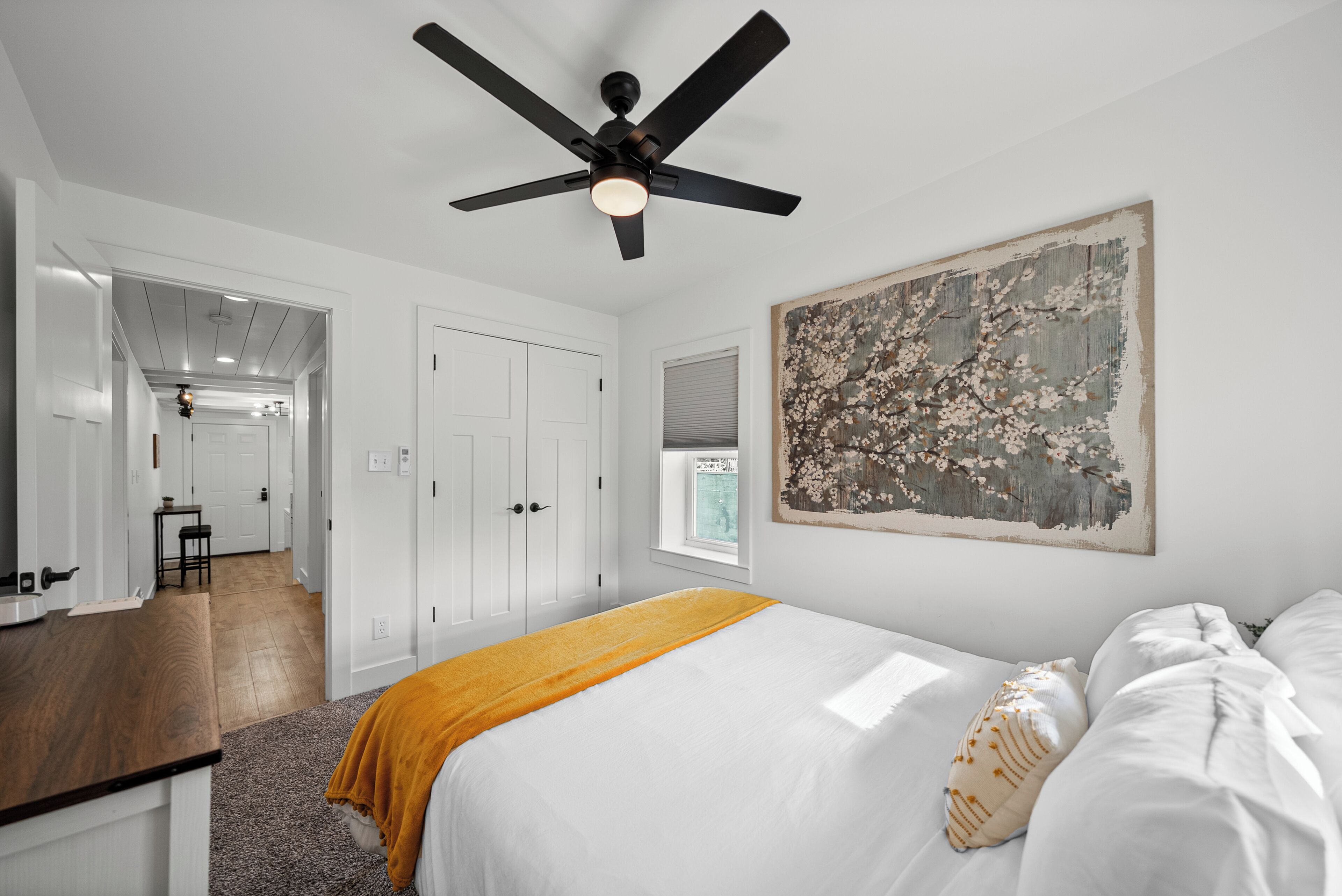 A bedroom with a bed, a ceiling fan, a window, and a door leading to another room.