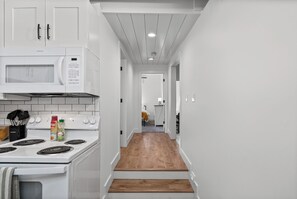 A kitchen with white cabinets, a microwave, stove, and wooden flooring.