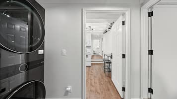 A hallway with a modern kitchen area, a dining table, and a black appliance.