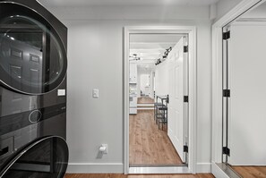 Un couloir qui donne sur un espace cuisine moderne, une table à manger et un appareil électroménager noir.