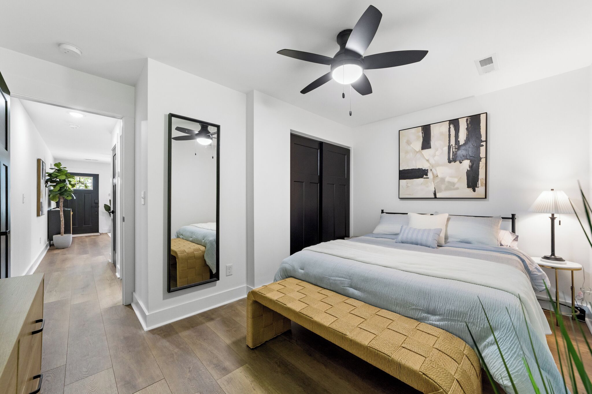 A modern bedroom with a bed, bedside table, lamp, and a ceiling fan.