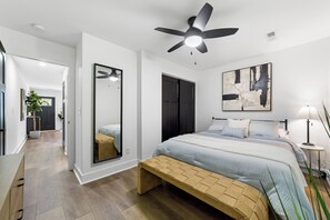 A modern bedroom with a bed, bedside table, lamp, and a ceiling fan.