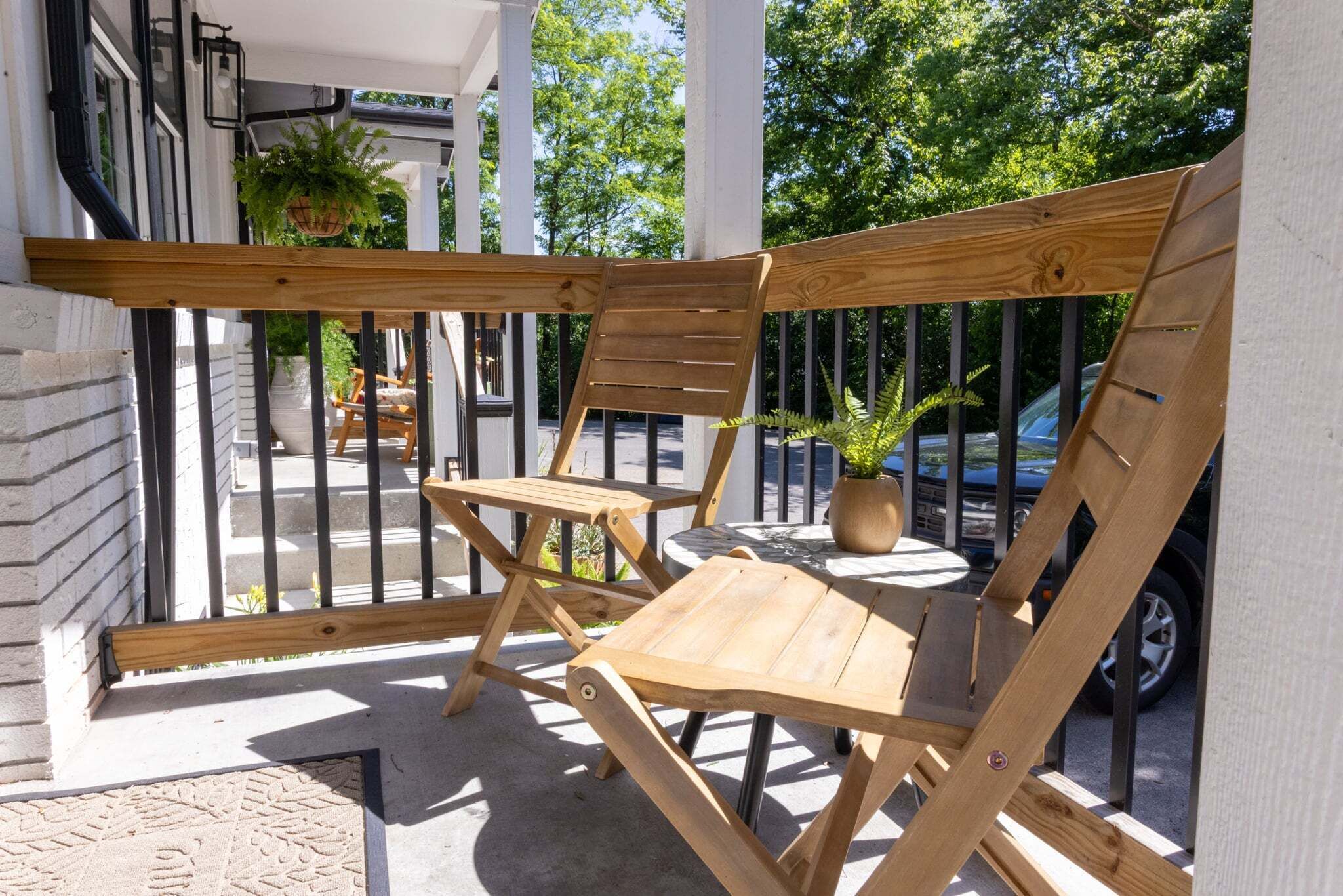 A wooden outdoor seating area with chairs and a table, a potted plant, and a car in the background.
