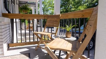 A wooden outdoor seating area with chairs and a table, a potted plant, and a car in the background.