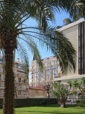 Ein Gebäude mit Balkonen, einer Palme und einer Hecke.