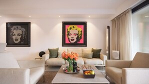 Uma sala de estar moderna com dois sofás, uma mesa de centro com flores e frutas, e duas obras de arte emolduradas na parede.