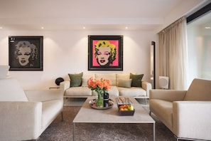 Ein modernes Wohnzimmer mit zwei Sofas, einem Couchtisch mit Blumen und Früchten sowie zwei gerahmten Kunstwerken an der Wand.