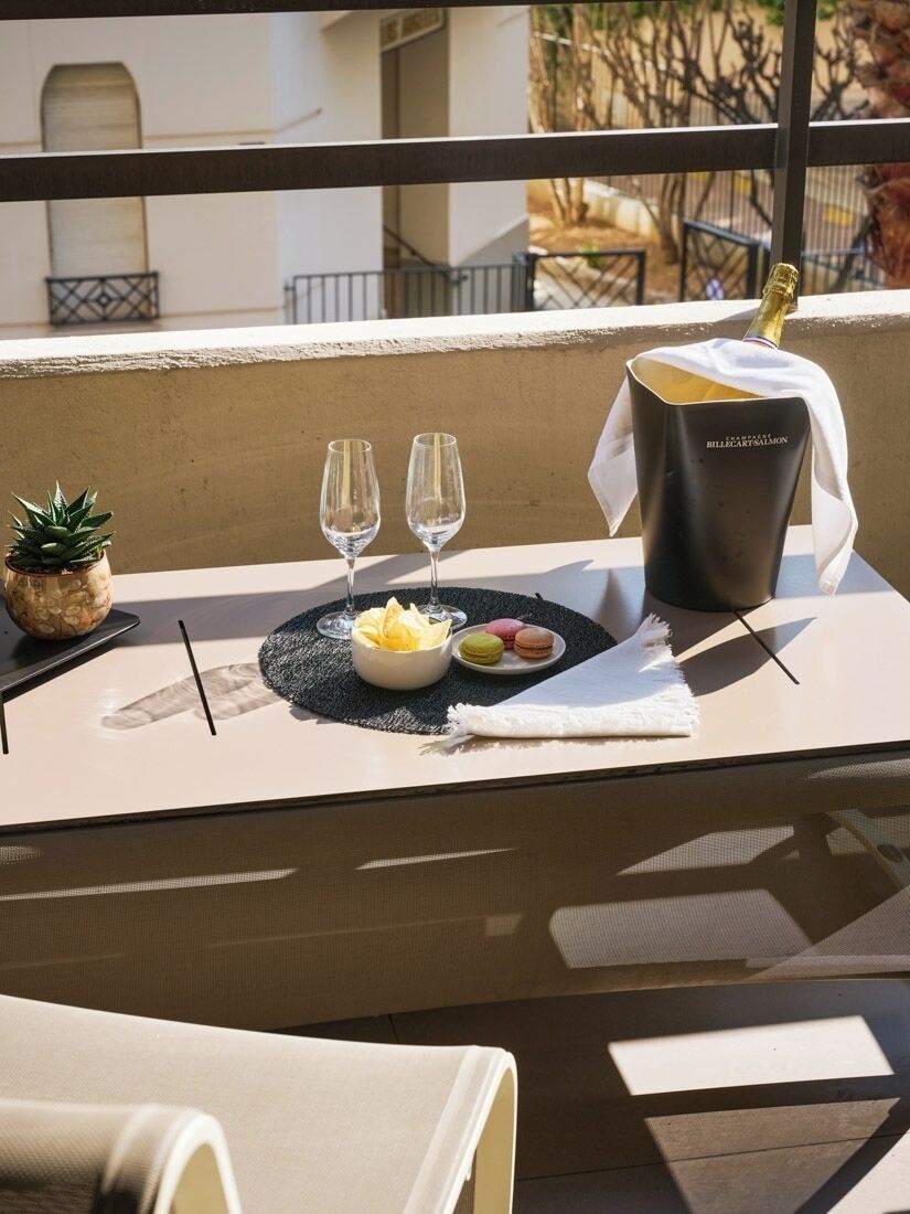 A table set with two glasses, a bottle of champagne, and a plate of macarons on a balcony.