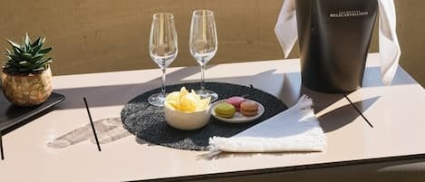 A table set with two glasses, a bottle of champagne, and a plate of macarons on a balcony.