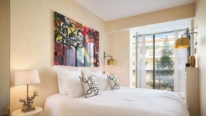 A bedroom with a large bed, a window with curtains, a wall art piece, and a bedside lamp. - Upstays Croisette 75m² 2Br with terasse (Cannes)