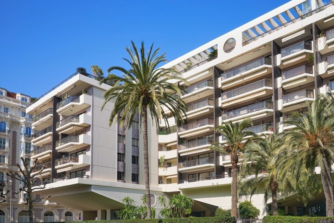 Un hotel de diverses plantes amb balcons, palmeres i un cel blau clar.