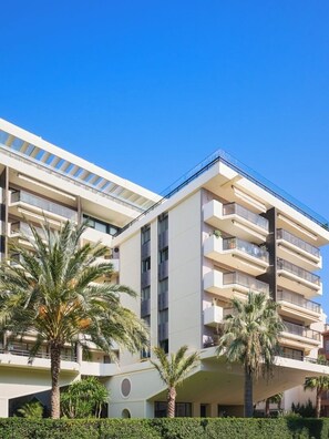 Ein mehrstöckiges Hotel mit Balkonen, Palmen und blauem Himmel.