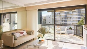 A modern living room with a sofa, coffee table, and a balcony with a view of a residential building. - Upstays Croisette 75m² 2Br with terasse (Cannes)