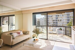 Uma sala de estar moderna com sofá, mesa de centro e uma varanda com vista para um prédio residencial.