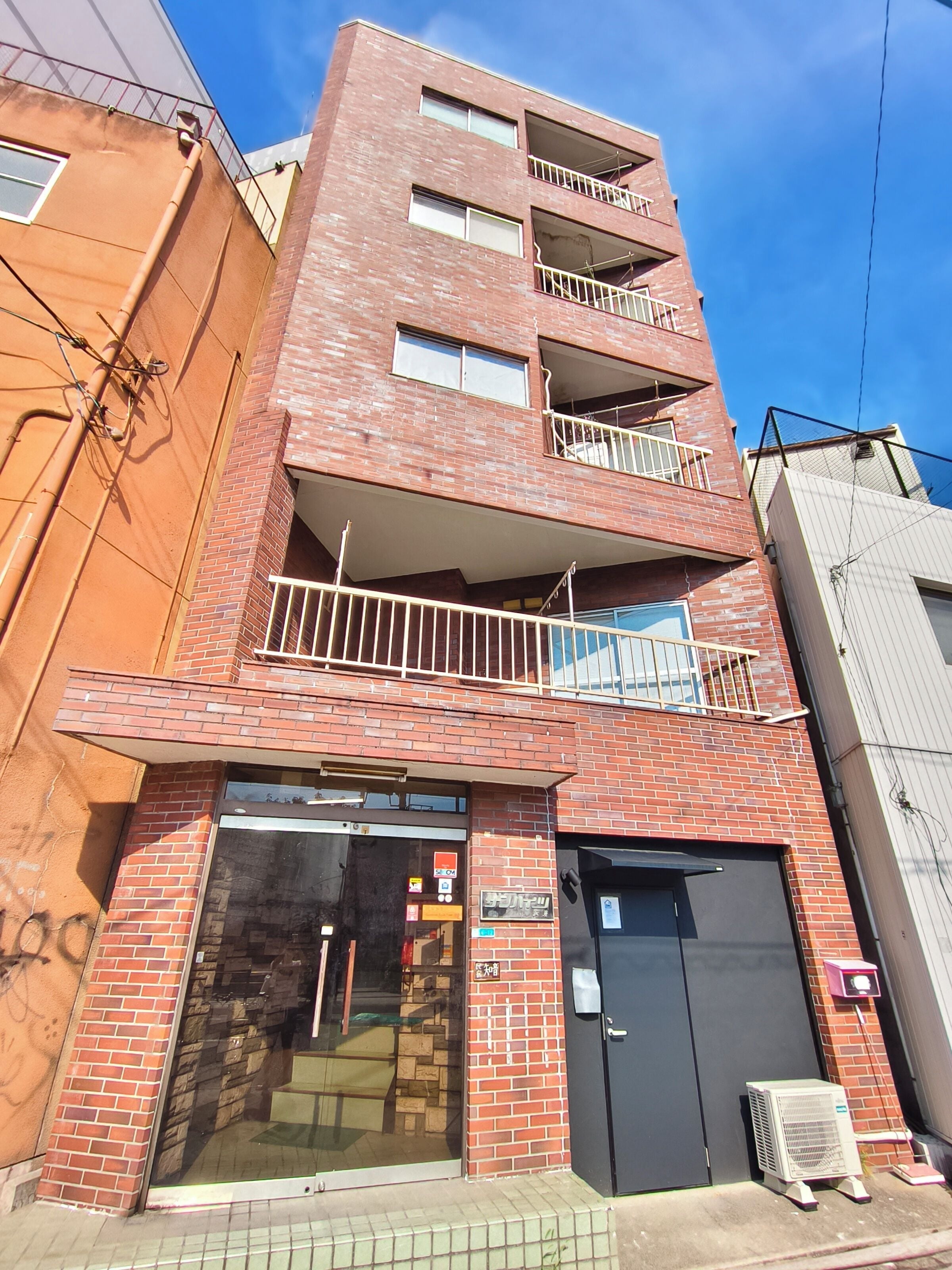 A multi-story building with a brick facade, a ground-level entrance, and a visible air conditioning unit outside.