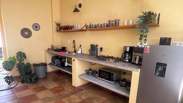 Eine Küche mit Gasherd, Mikrowelle und Kühlschrank. Es gibt Regale mit Geschirr und einen Blumentopf.