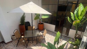 Ein überdachter Patio-Bereich mit Tisch, Stühlen, Topfpflanzen und einem großen Sonnenschirm.