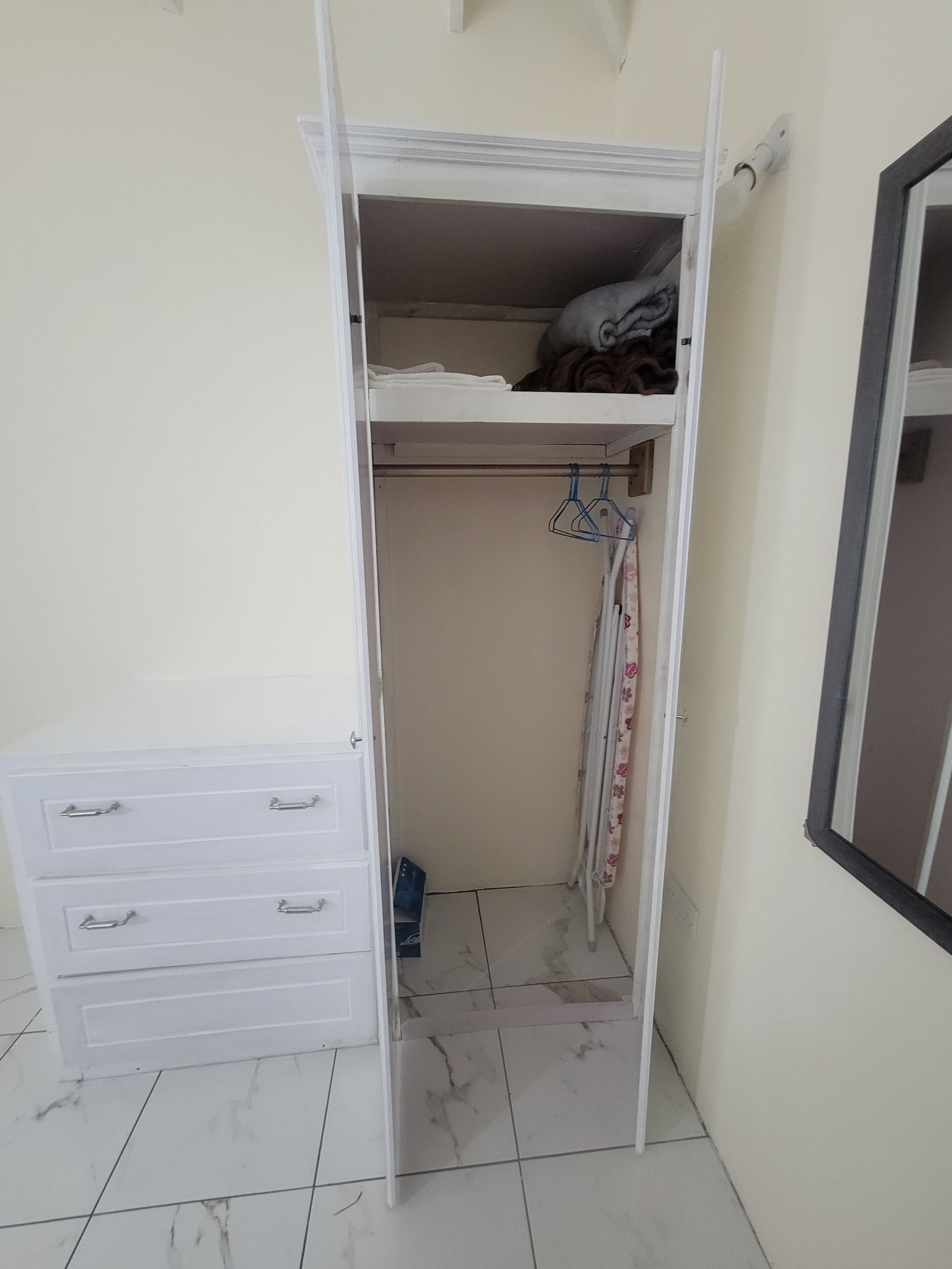 A white closet with a lower shelf, a hanging rack, and a small drawer unit.