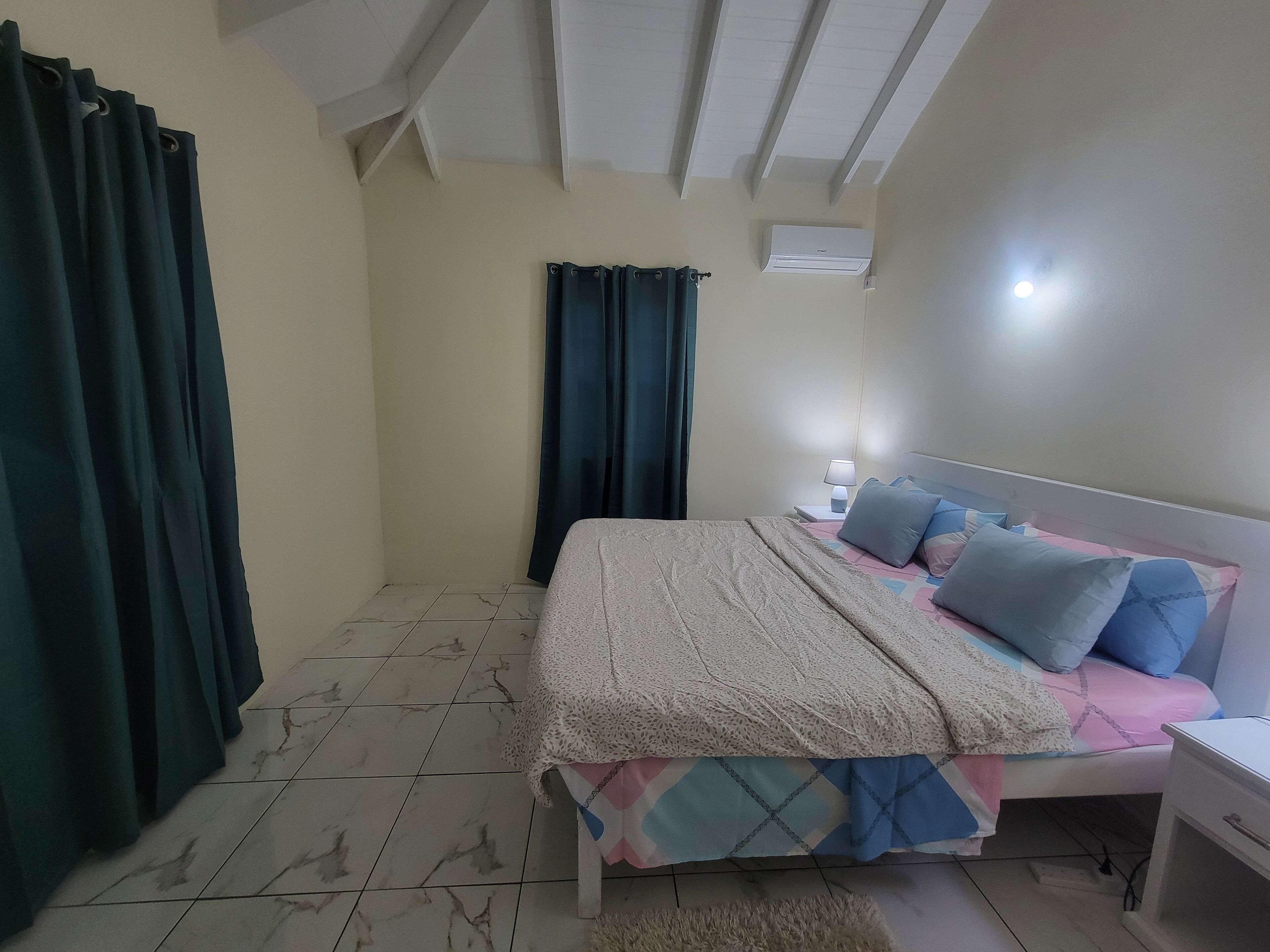 A bedroom with a bed, a nightstand, a lamp, and an air conditioning unit.