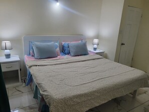 A bedroom with a bed, two bedside tables, a nightstand, a door, and a wall socket. - ​Country Green — A Peaceful Saint Lucian Countryside Getaway (Castries)