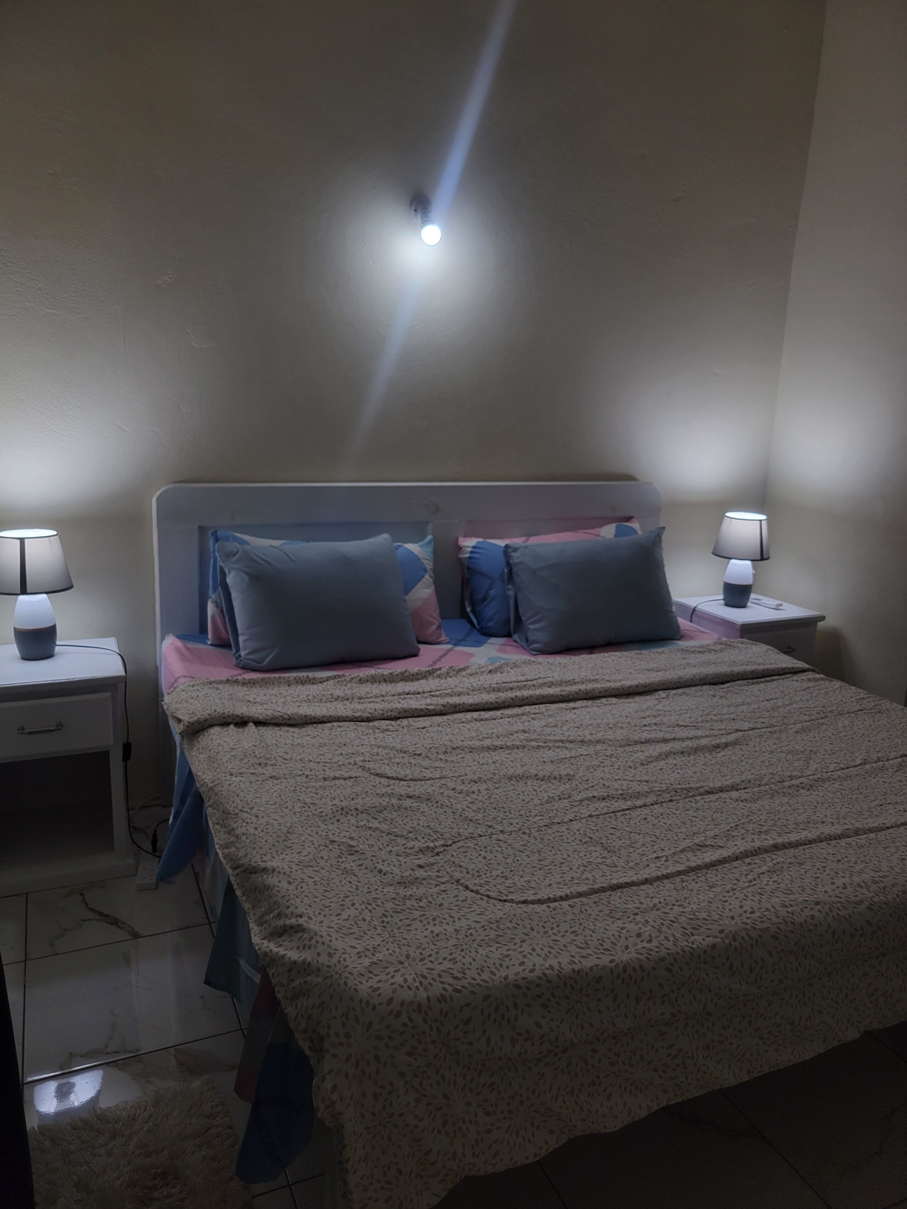 Une chambre à coucher avec un lit, deux tables de chevet et un luminaire au plafond.