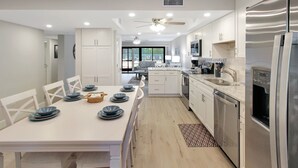 Una cucina moderna con mobili bianchi, un frigorifero in acciaio inossidabile e un'area pranzo con un tavolo bianco apparecchiato per sei persone.