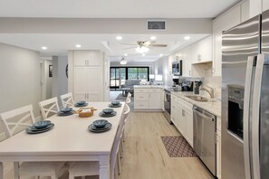Eine moderne Küche mit weißen Schränken, einem Edelstahlkühlschrank und einem Essbereich mit einem weißen Tisch, gedeckt für sechs Personen.