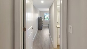 Un corridoio stretto con pareti bianche e pavimento in legno che conduce a un bagno con una finestra.