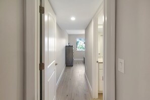 Ein schmaler Korridor mit weißen Wänden und Holzboden, der zu einem Badezimmer mit Fenster führt.