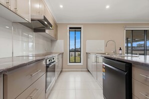 A modern kitchen with stainless steel appliances, a dishwasher, and a window providing a view of the outdoors. - Robinson Retreat - Sleeps 8, Pet Friendly (Orange)