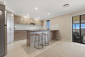 A modern kitchen with a central island, bar stools, and a sliding glass door leading to an outdoor area. - Robinson Retreat - Sleeps 8, Pet Friendly (Orange)