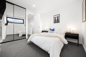 A modern bedroom with a large bed, a glass partition wall, and a framed picture on the wall.