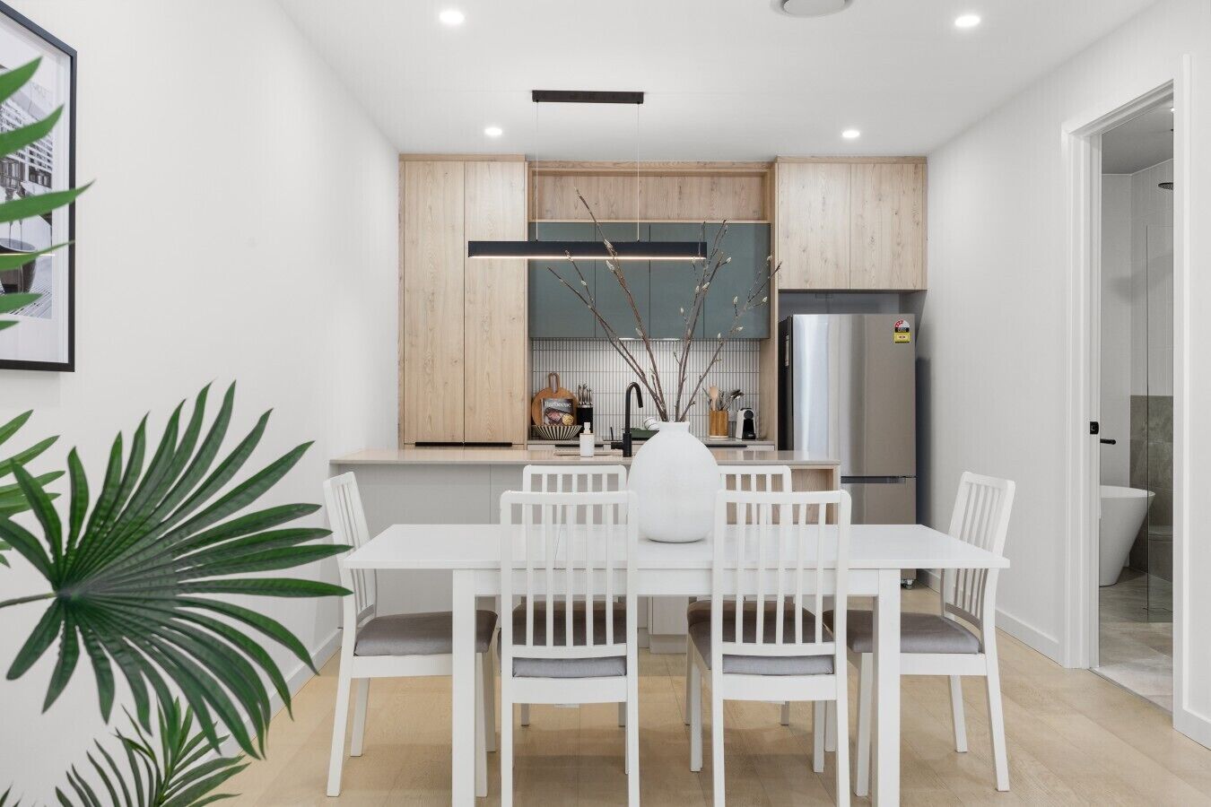 Une cuisine moderne avec des meubles en bois, un réfrigérateur en acier inoxydable et un coin repas comprenant une table et des chaises blanches.