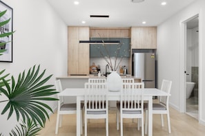 A modern kitchen with wooden cabinets, a stainless steel refrigerator, and a dining area with a white table and chairs.