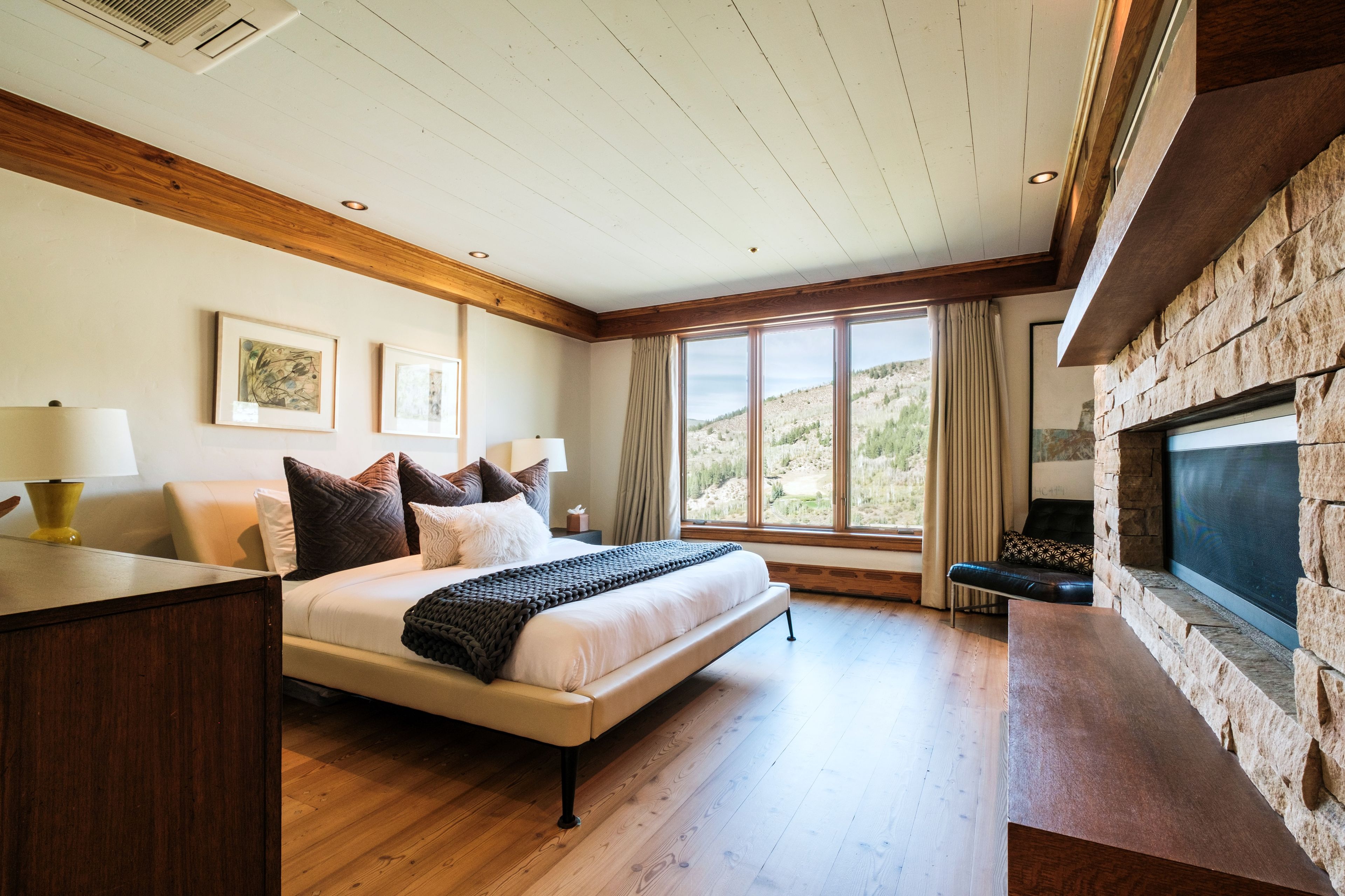 Un dormitorio con cama, escritorio, chimenea y un ventanal con vistas al exterior.