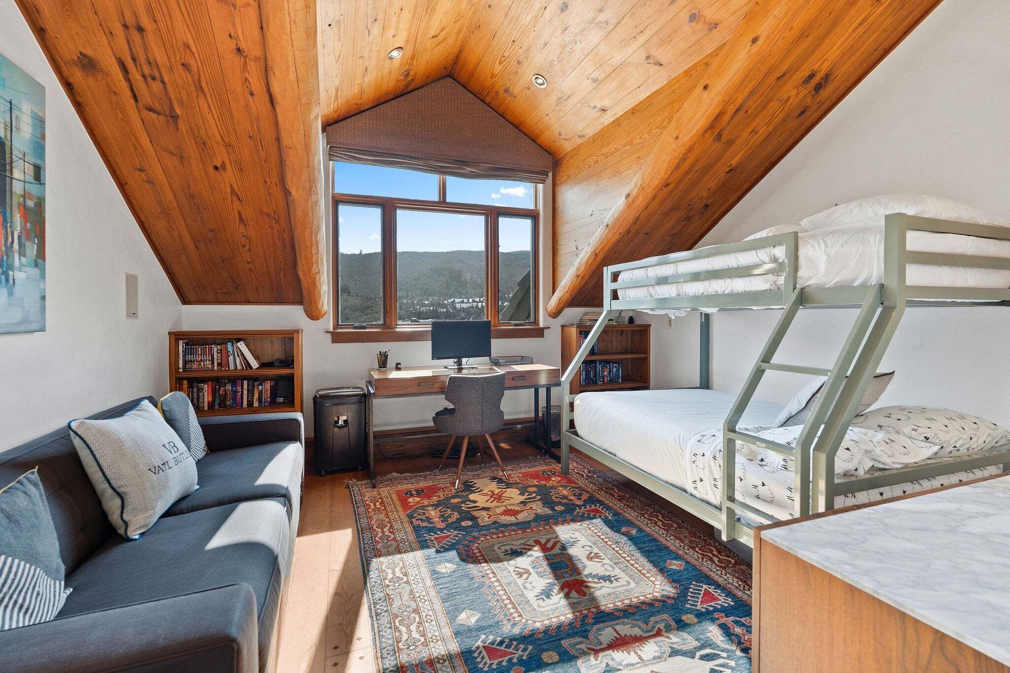 Un dormitorio ático acogedor con literas, un escritorio, una computadora, un sofá y un ventanal que ofrece vistas del paisaje.