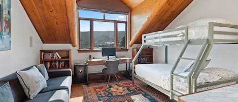 Un dormitorio ático acogedor con literas, un escritorio, una computadora, un sofá y un ventanal que ofrece vistas del paisaje.