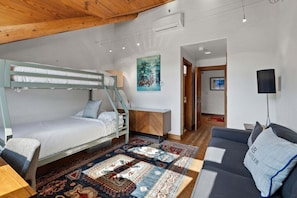 Ein Zimmer mit einem Etagenbett, einer Schlafcouch, einem gemusterten Teppich, einem Gemälde und einer Lampe.