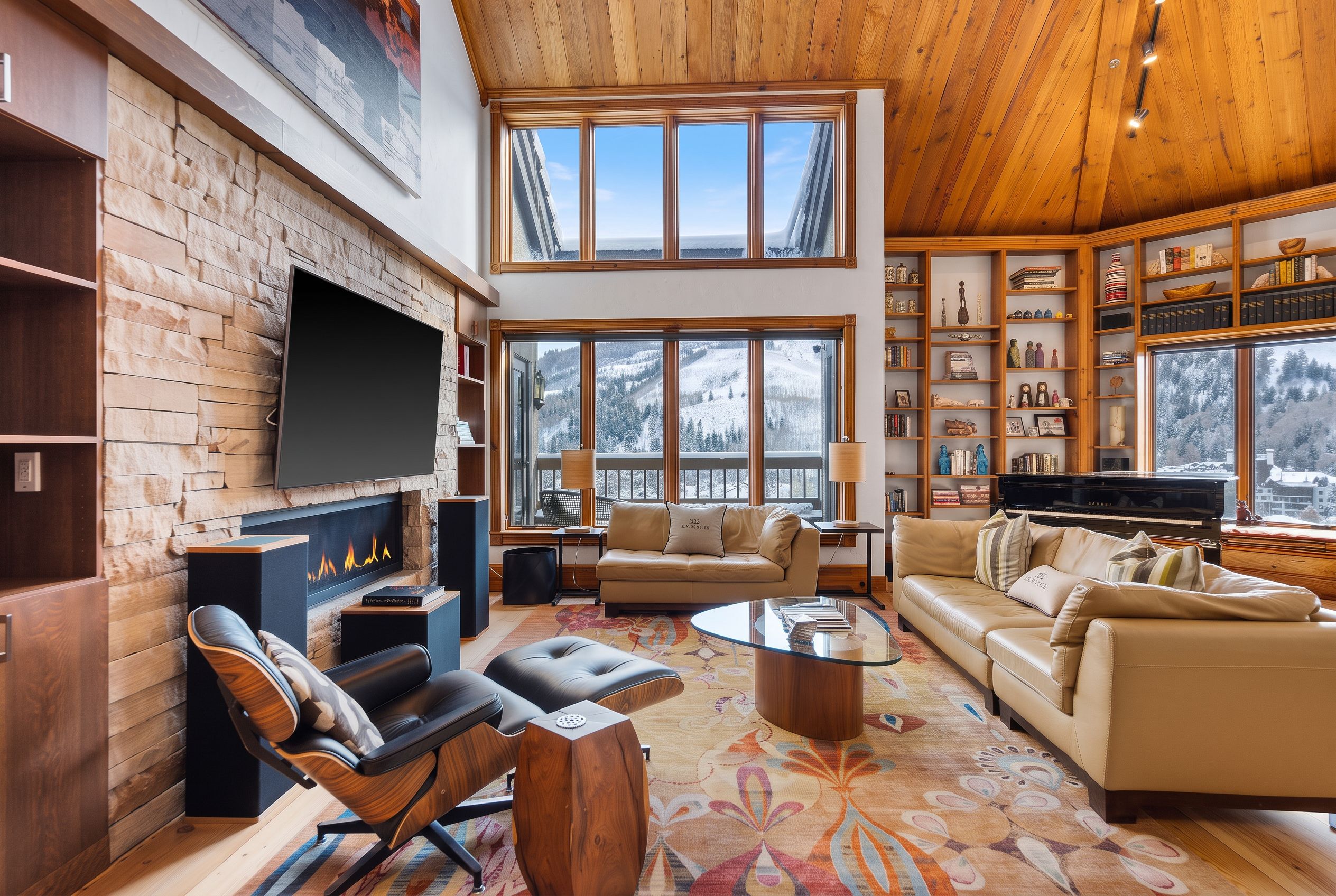 A spacious living room with a fireplace, leather sofas, a coffee table, and a large bookshelf filled with books and decorative items.