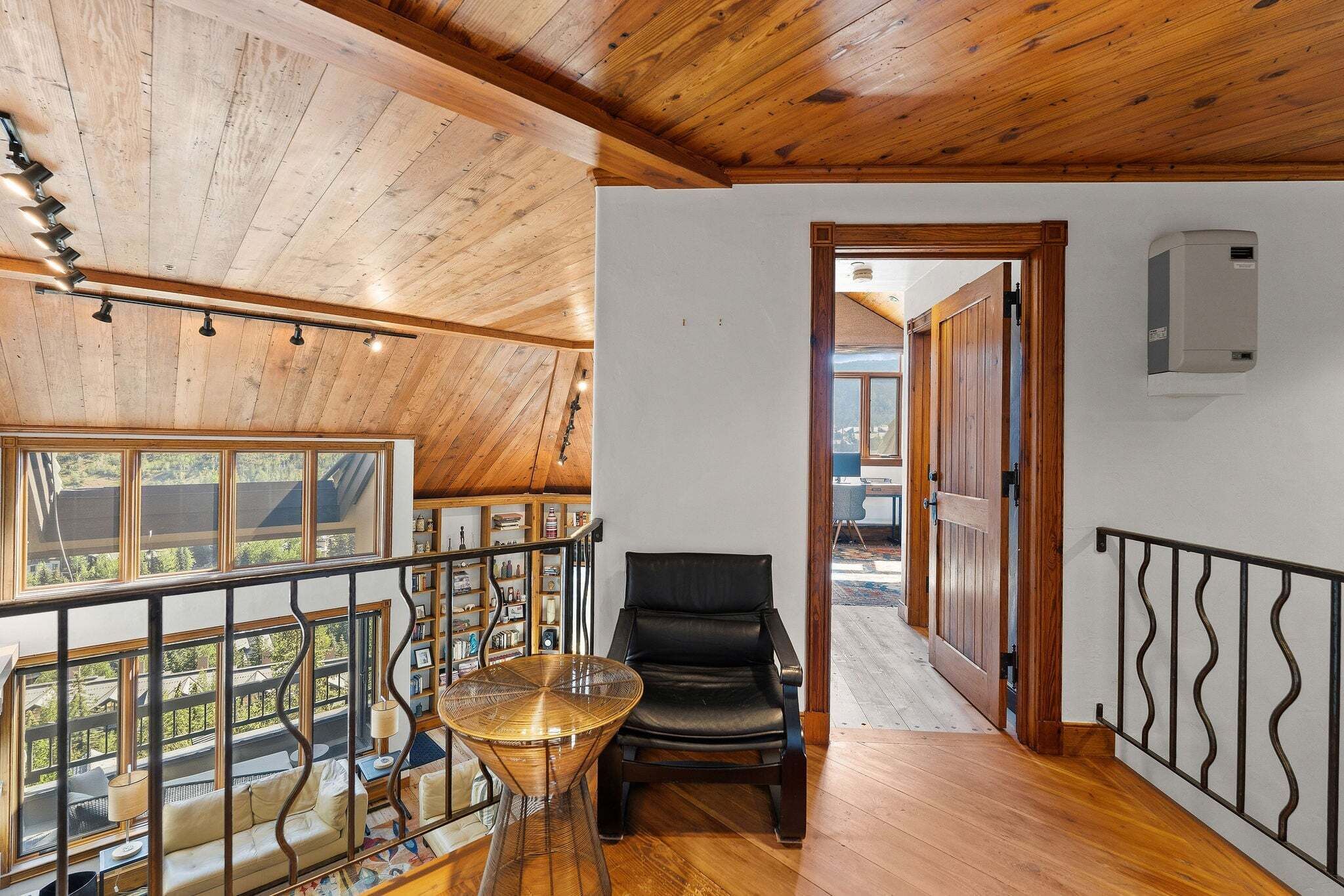 Una habitación amplia con techo alto, vigas de madera, un balcón con barandilla, una mesa de comedor con sillas y vistas al exterior.