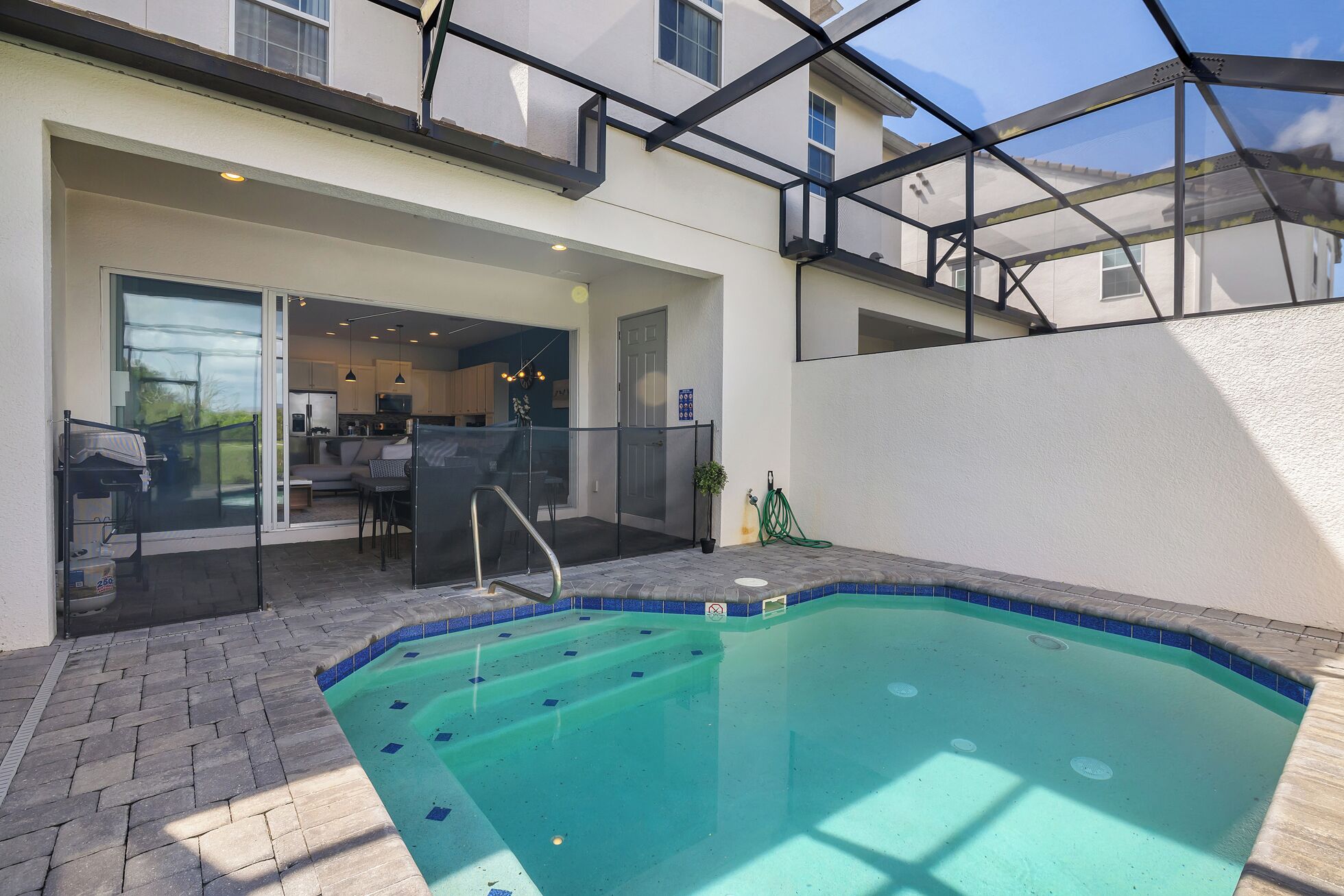 Una piscina con cerramiento de vidrio, un patio con mobiliario exterior y vista al edificio contiguo.