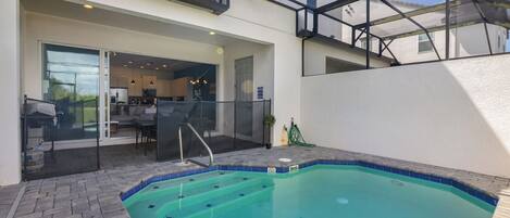 Une piscine entourée de parois en verre, un espace patio aménagé avec du mobilier d’extérieur et une vue sur l’immeuble voisin.