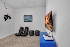 A room with a large flat-screen TV, a gaming controller, two massage chairs, a painting, and a blue desk with a remote control. - 4BR Family Townhome, pool, resort & Splash (Davenport)